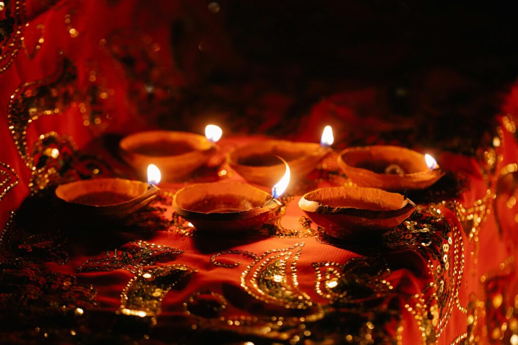 Traditional oil lamps glow warmly on vibrant red and gold fabrics, creating a festive ambiance.
