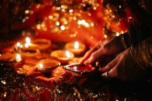 Hands lighting candles during a vibrant Indian festival ceremony.